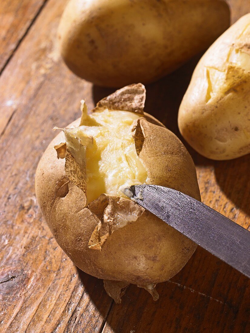 Boiled potatoes with knife on wooden background
