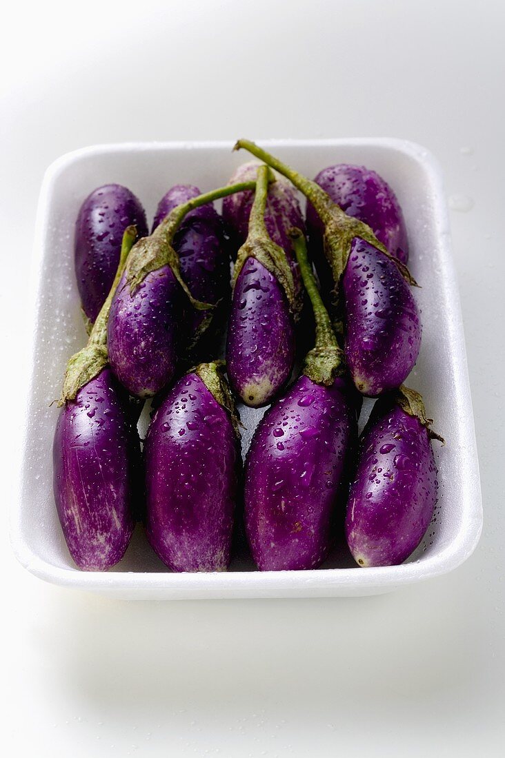 Baby aubergines with drops of water in white dish