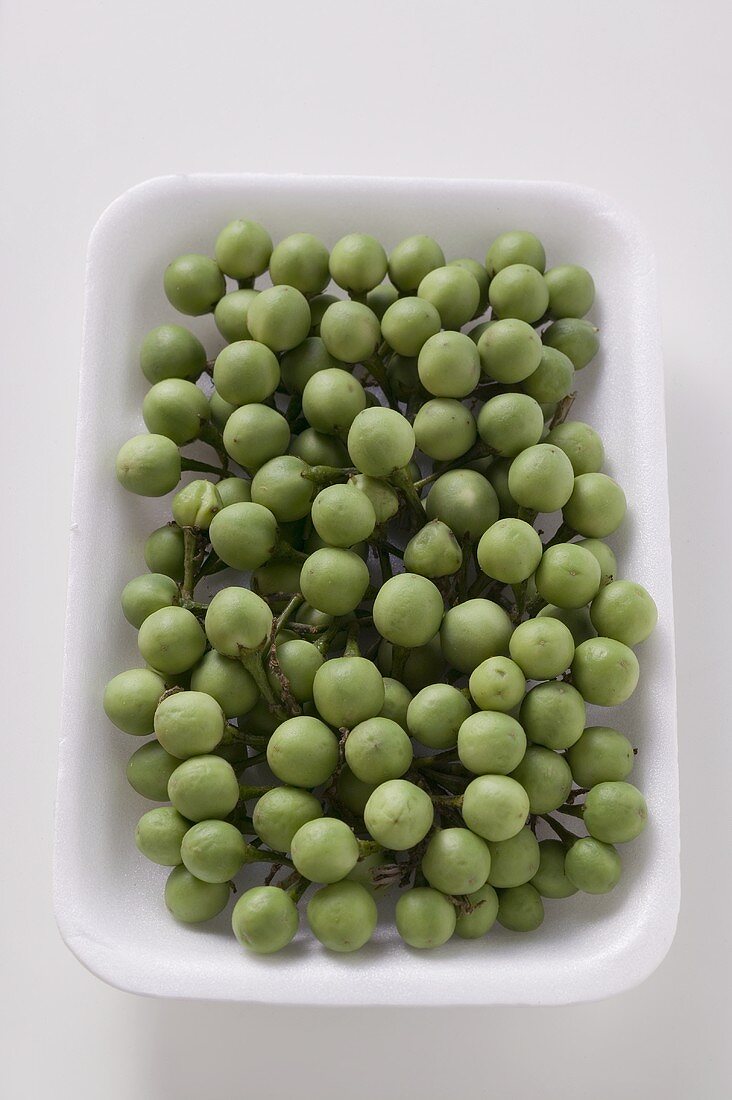 Green baby aubergines in white dish