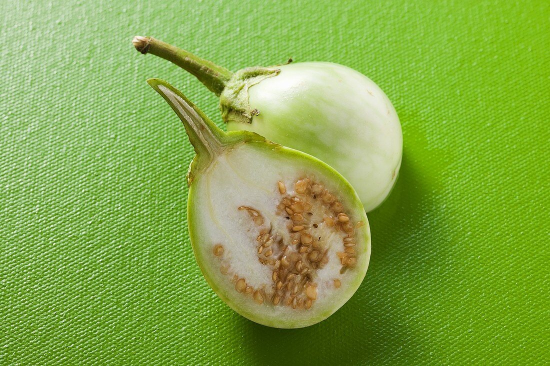 Green baby aubergine, halved, on green background