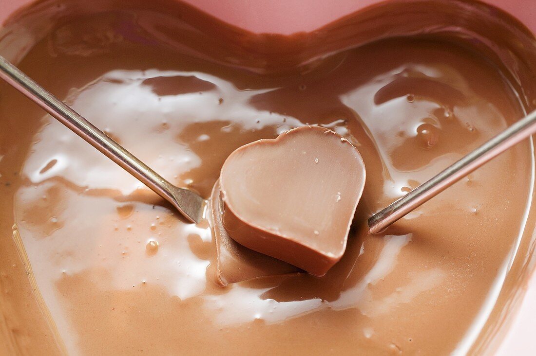 Schokoladenfondue mit Herzpraline auf zwei Fonduegabeln