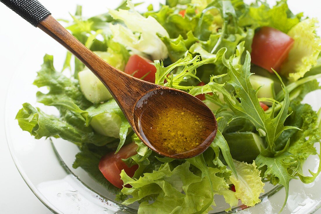 Olive oil in wooden spoon above salad leaves