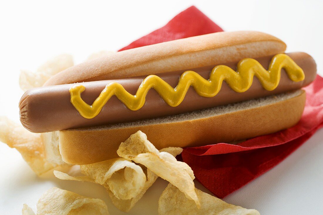 Hot dog with mustard and potato crisps on red napkin