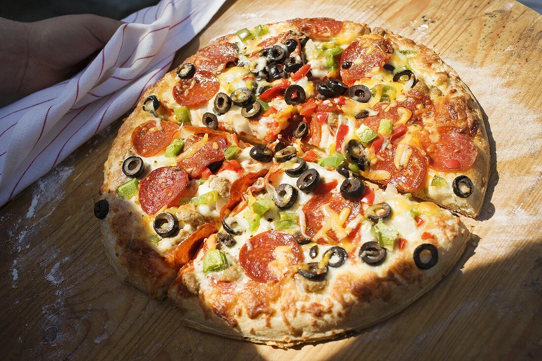 Hand hält Pizza mit Peperoniwurst, Paprika und Oliven