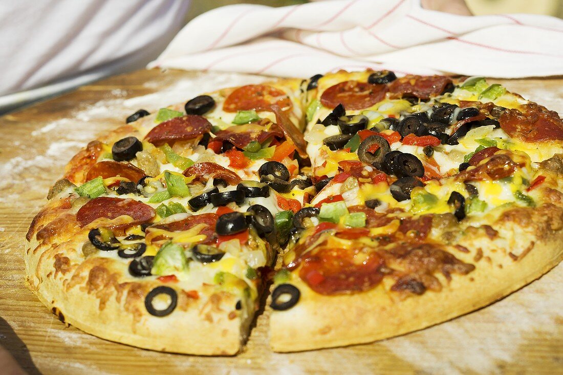 Person holding pepperoni pizza with peppers and olives