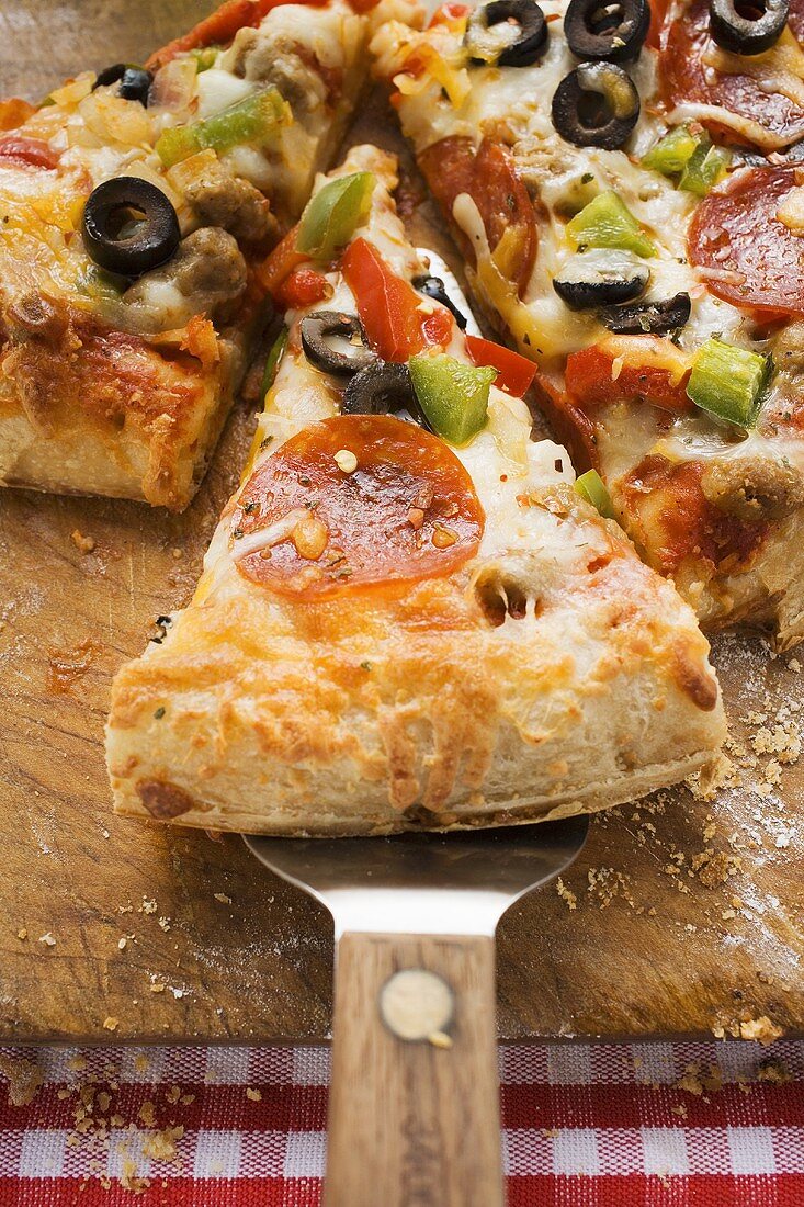 Stück Pizza mit Peperoniwurst, Paprika und Oliven auf Heber