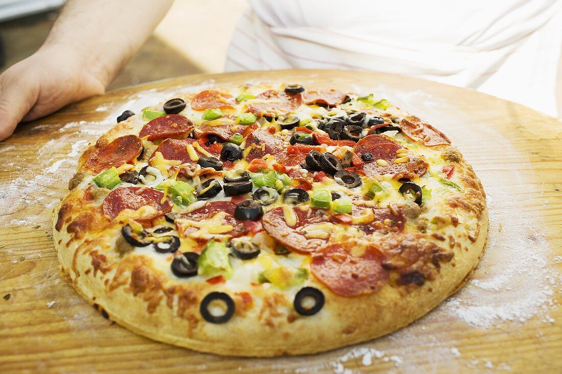 Hände halten Pizza mit Peperoniwurst, Paprika und Oliven