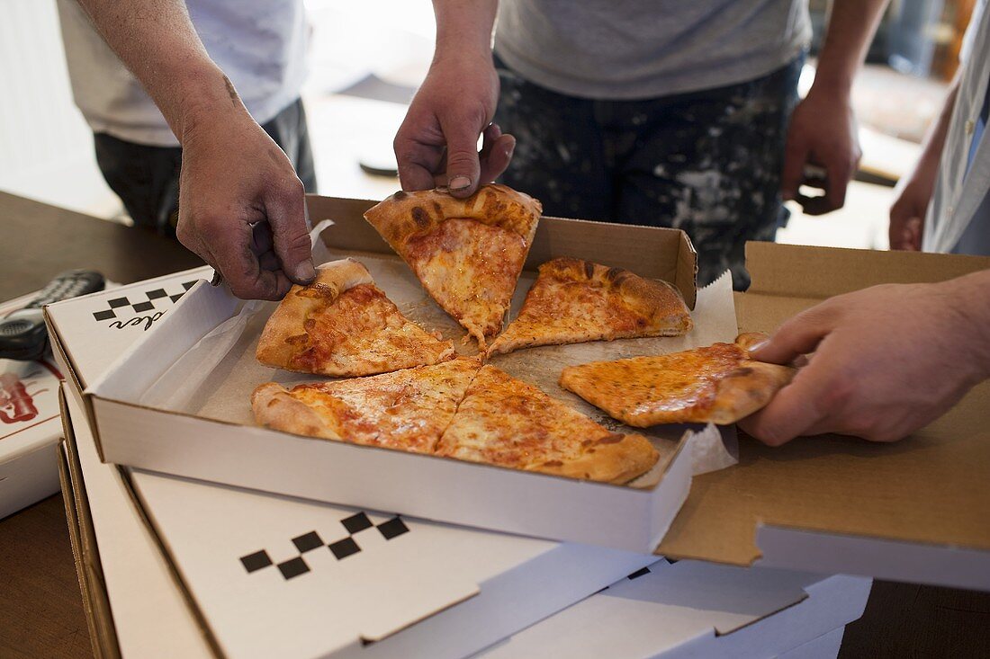 Workers taking pieces of pizza out of pizza box