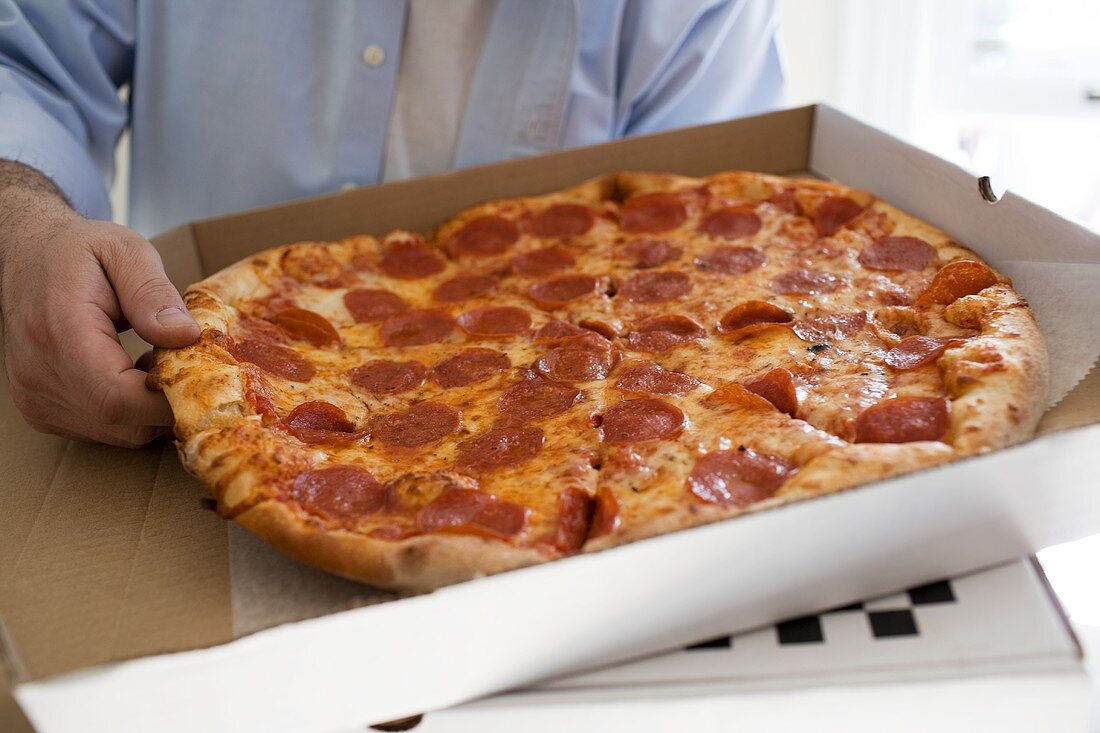 Man holding pizza box containing pepperoni pizza