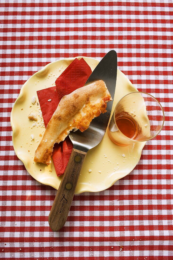 Teller mit Pizzarest, Papierserviette, Heber und Glas