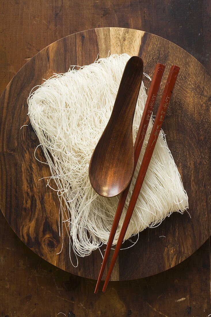 Dünne Reisnudeln auf Holzteller mit Essstäbchen und Löffel