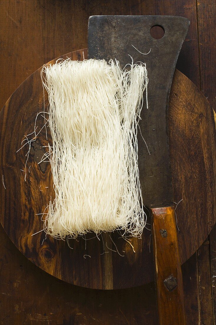 Dünne Reisnudeln auf Holzteller mit asiatischem Küchenbeil