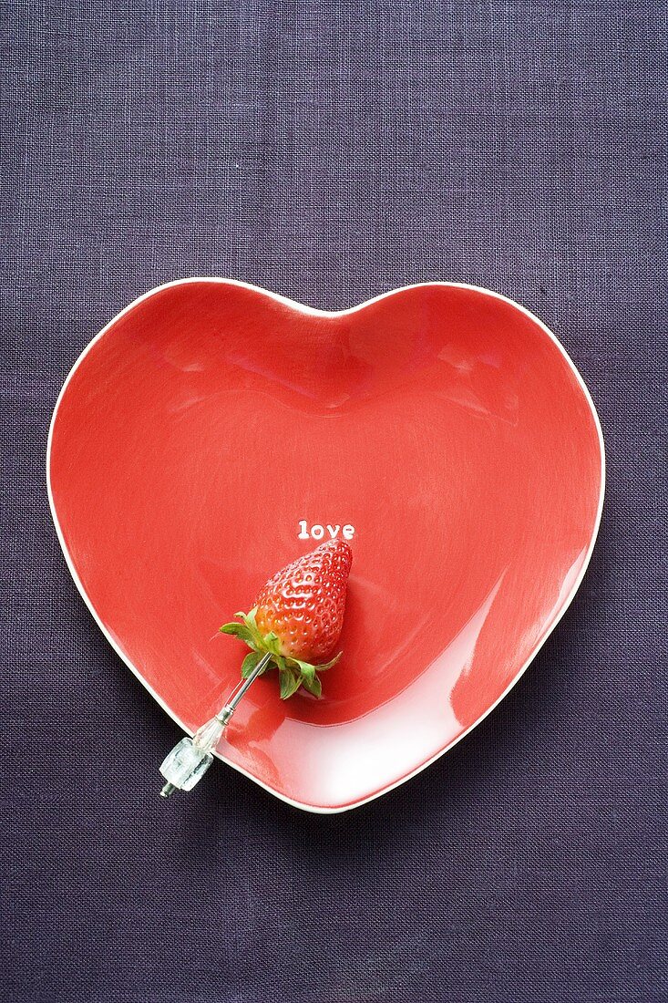 Strawberry on skewer on red heart-shaped plate