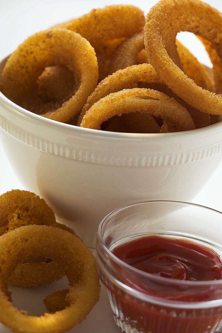 Deep-fried onion rings in white bowl, ketchup