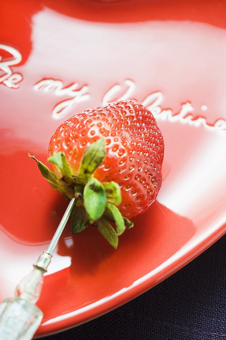 Erdbeere am Spiess auf rotem Teller zum Valentinstag