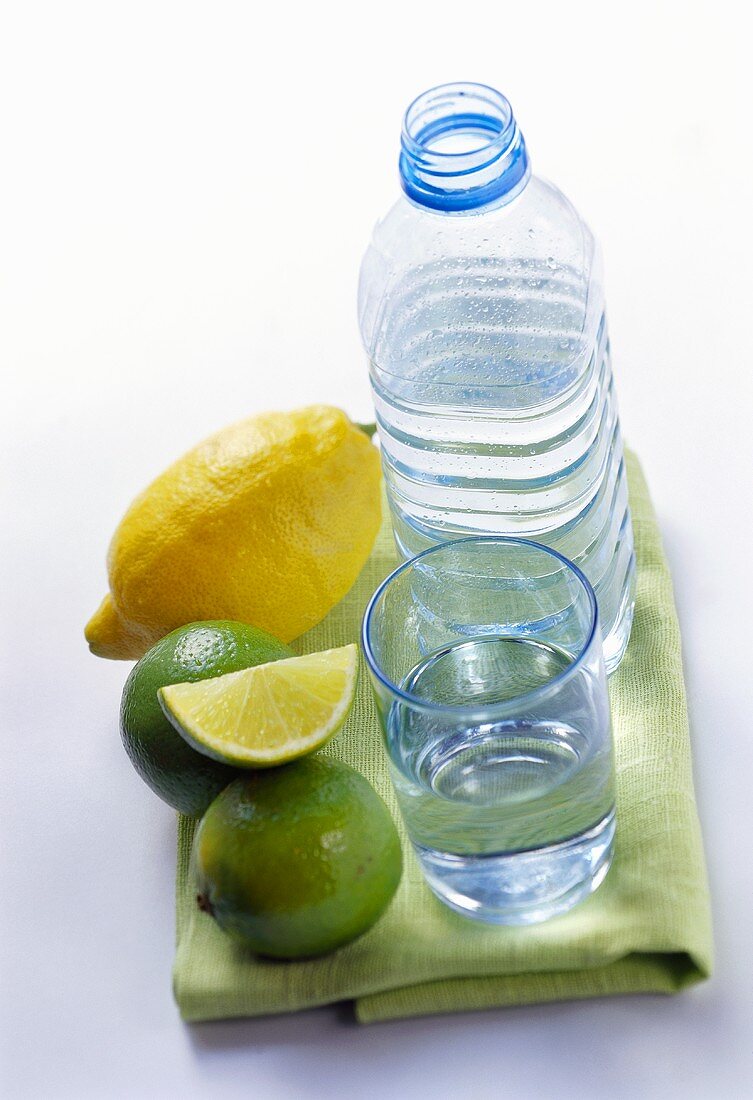 Still water in bottle and glass beside lemon and limes