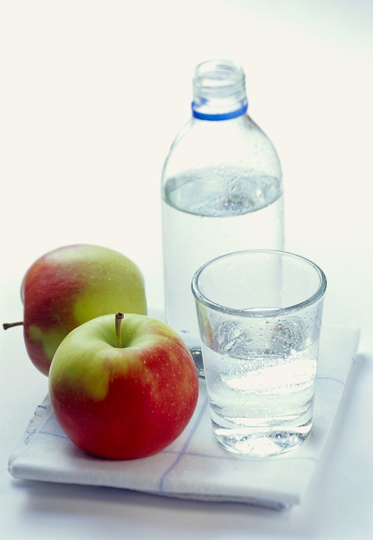 Eine Flasche und ein Glas mit Mineralwasser, daneben Äpfel