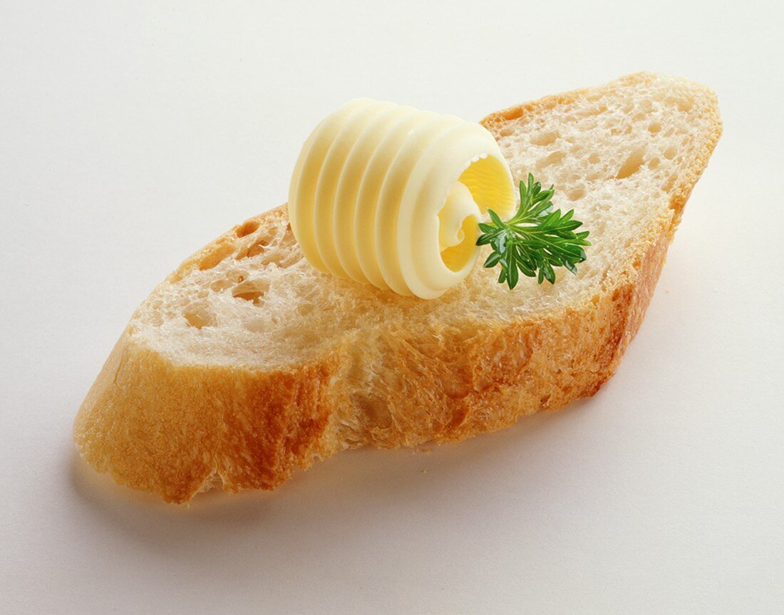 A slice of baguette with butter curl and parsley