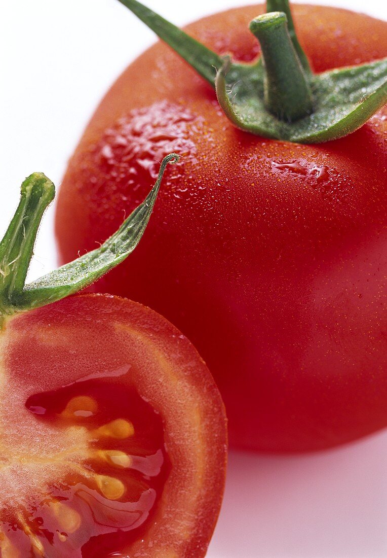 Tomate, ganz und halbiert, mit Wassertropfen