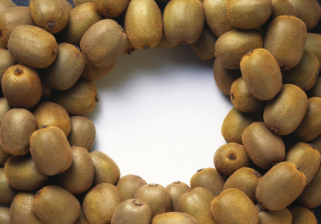 Lots of whole kiwi fruits, arranged around edge of picture