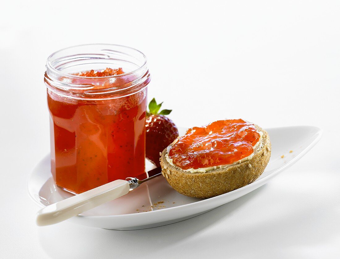Strawberry jam on bread roll and in jar