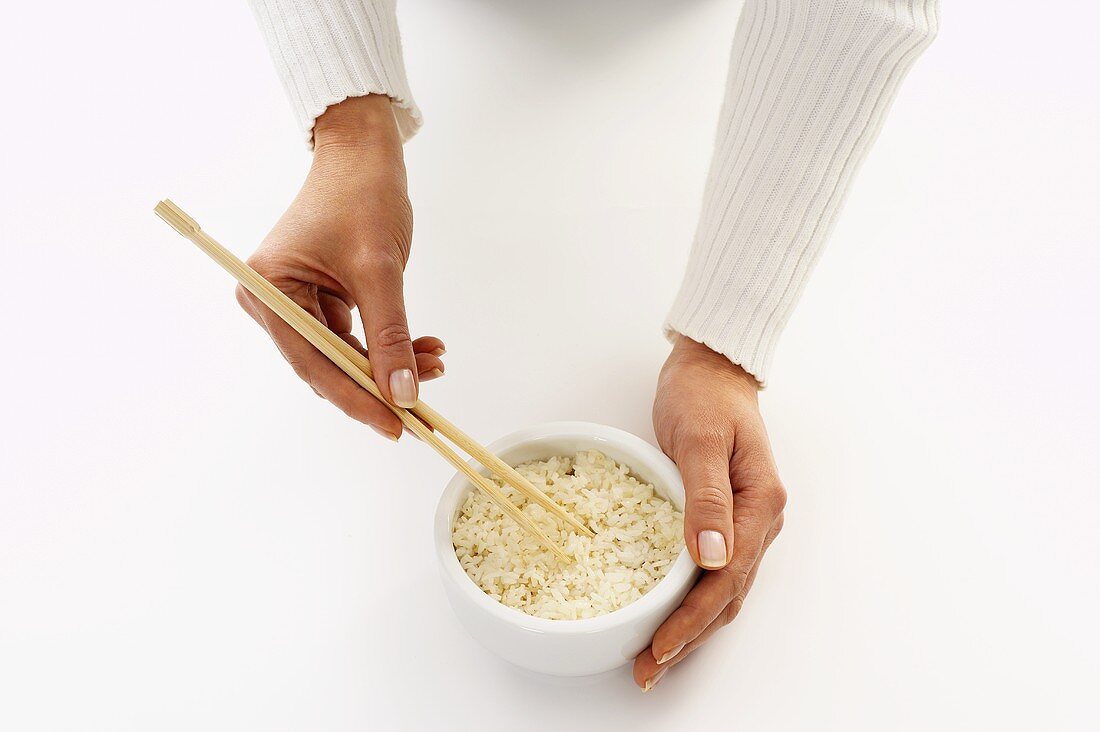 Frauenhände halten Stäbchen in eine Reisschüssel