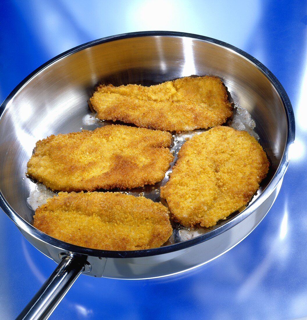 Four breaded pork escalopes being fried in a frying pan