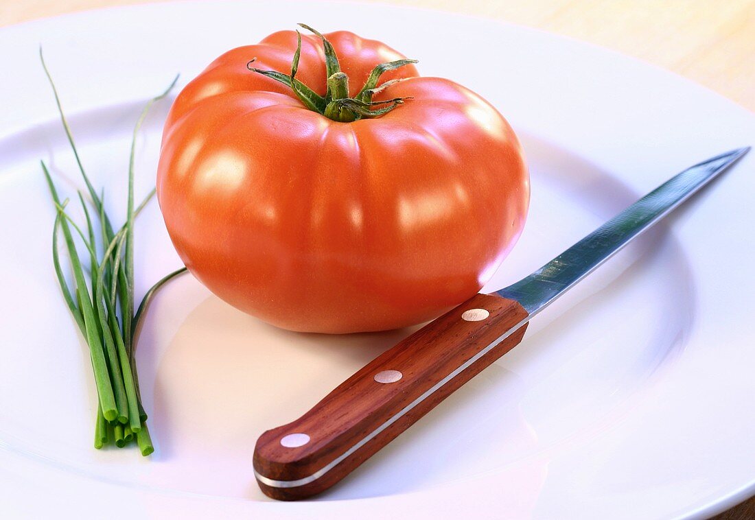 Eine Tomate, Schnittlauch und ein Messer auf einem Teller