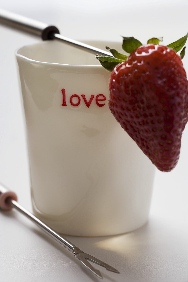 Becher mit 'love' Aufschrift und Fonduegabel mit Erdbeere