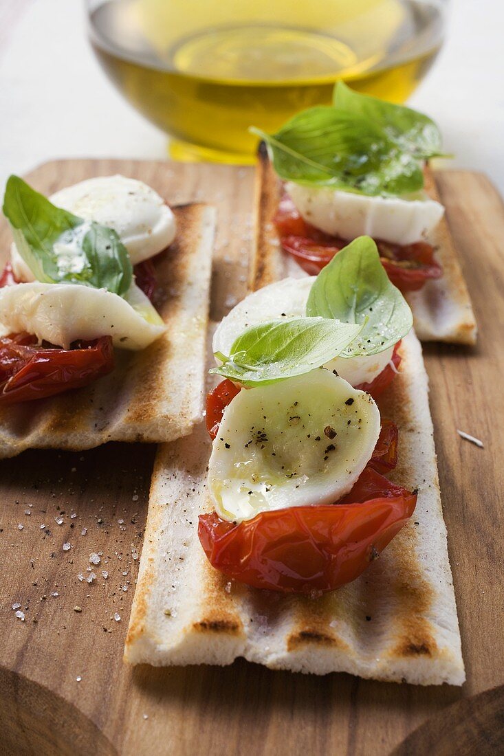 Gegrilltes Brot mit Tomaten und Mozzarella, dahinter Olivenöl