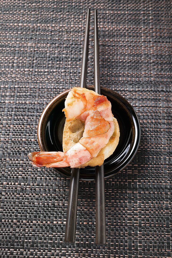 Bacon-wrapped king prawn on white bread and chopsticks
