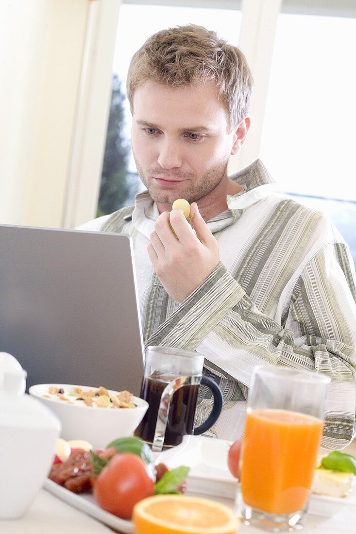 Junger Mann am Laptop beim Frühstücken