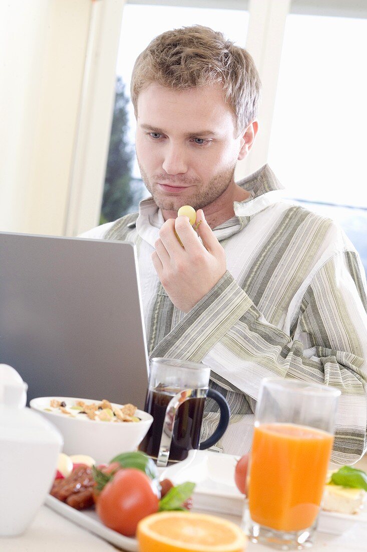 Young man at breakfast with laptop