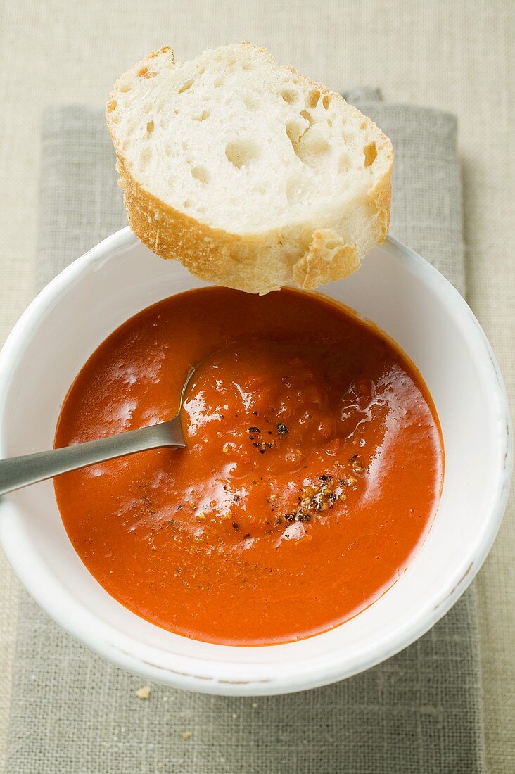 Paprikacremesuppe in Suppenschale, Löffel und Baguettescheibe