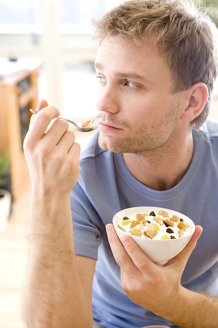 Junger Mann isst Joghurt-Beeren-Müsli