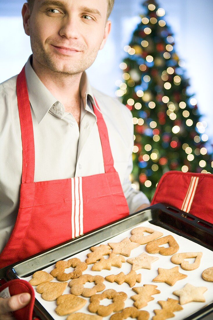 Man holding baking tray of Christmas biscuits