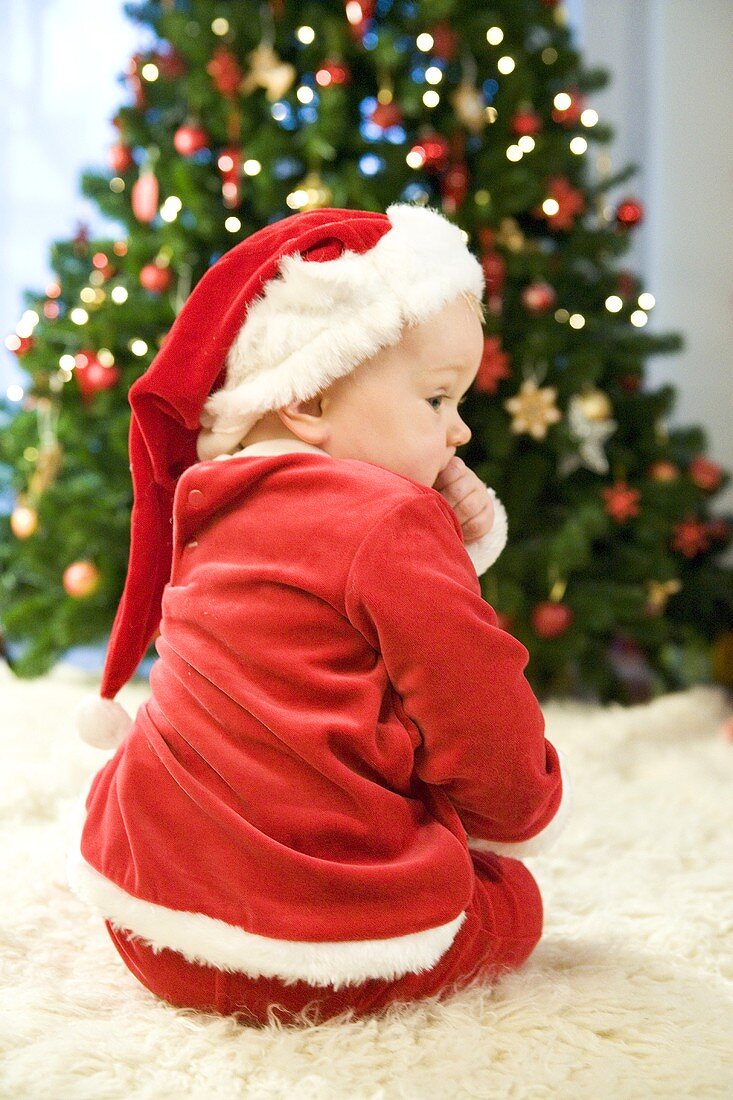 Small boy in Father Xmas costume sitting by Christmas tree