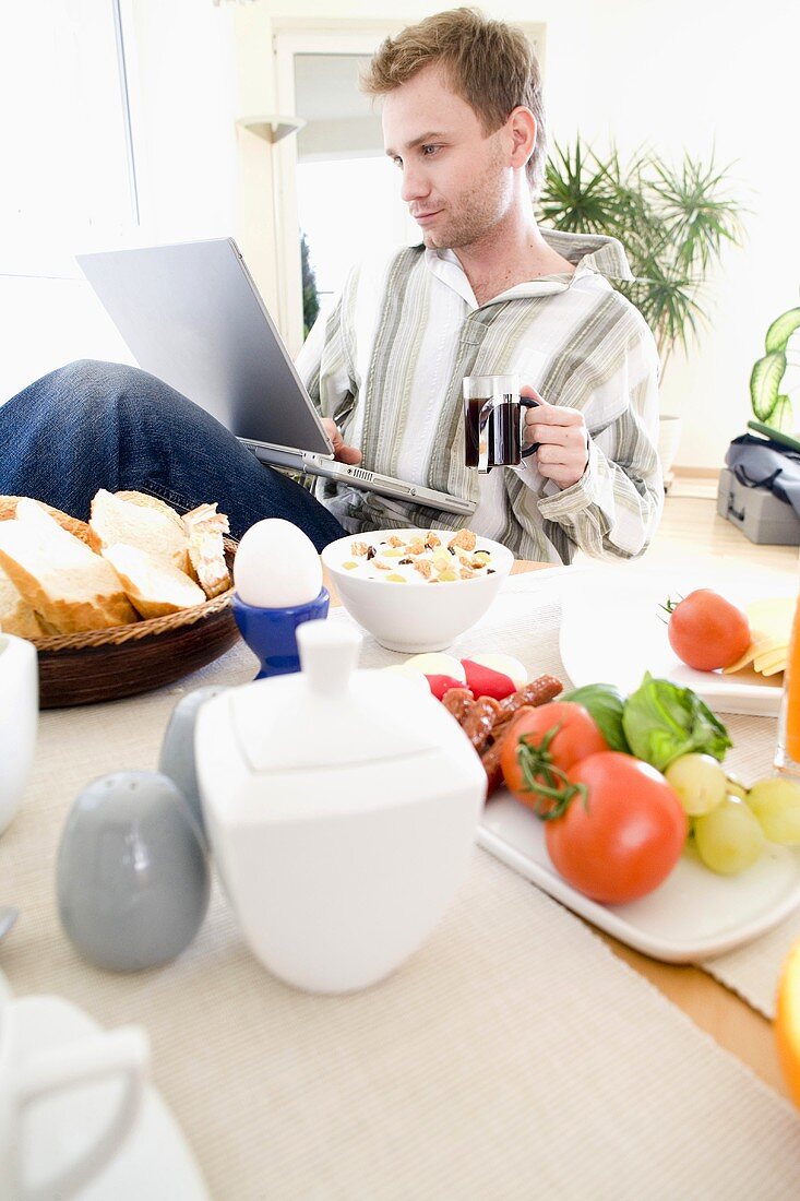 Junger Mann mit Laptop am Frühstückstisch