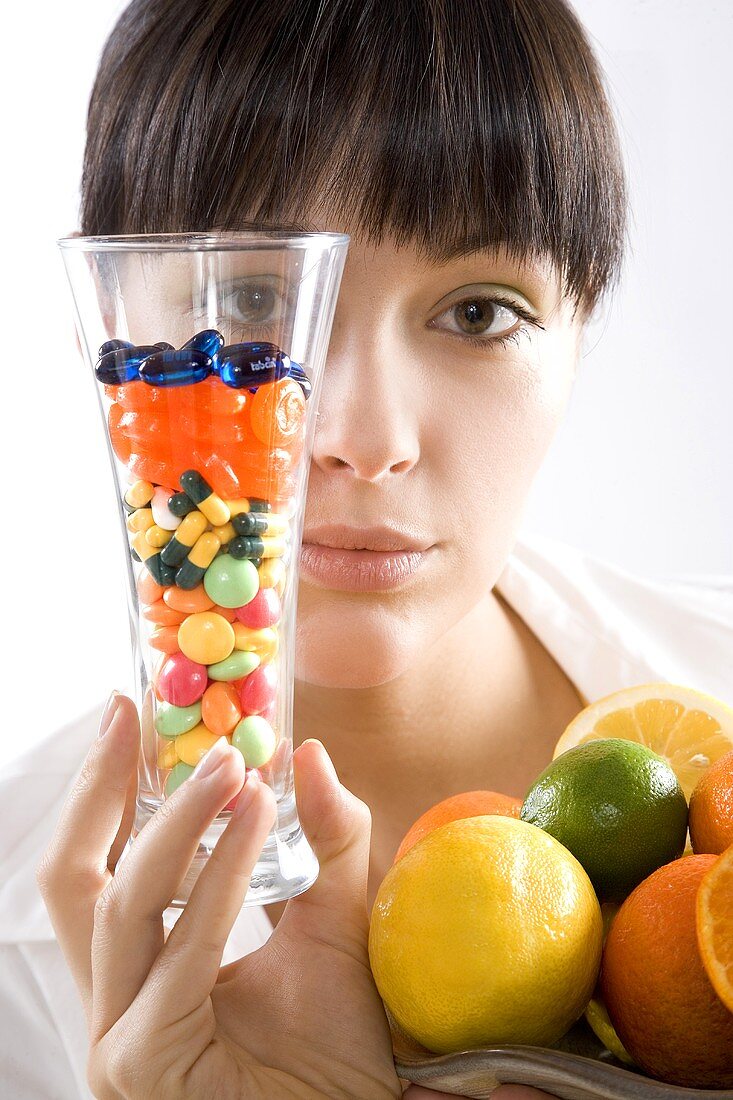 Young woman with vitamin pills and citrus fruit