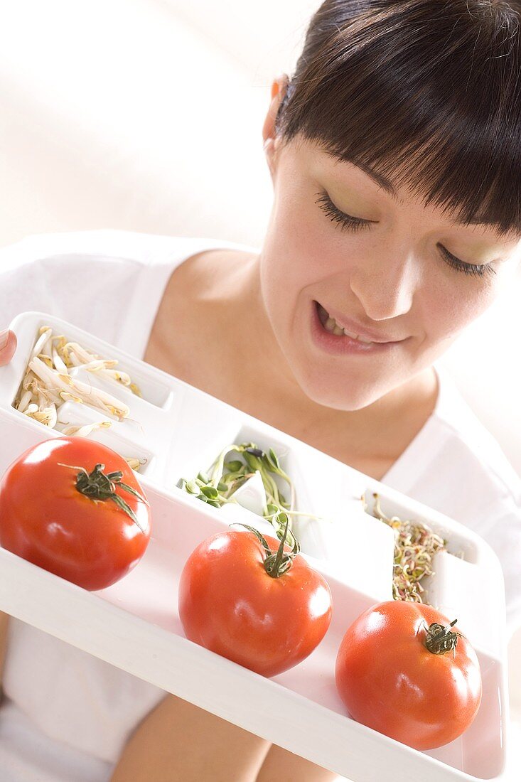 Young woman holding a plate of tomatoes and sprouts