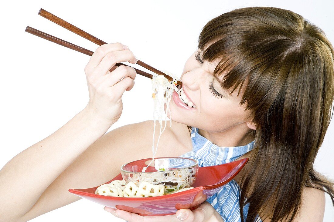 Young woman eating Asian noodle dish with chopsticks