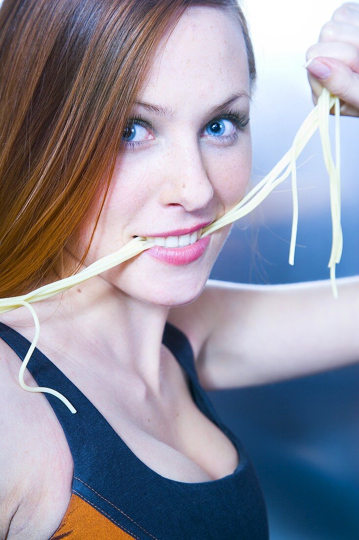 Sportliche junge Frau hält Spaghetti im Mund