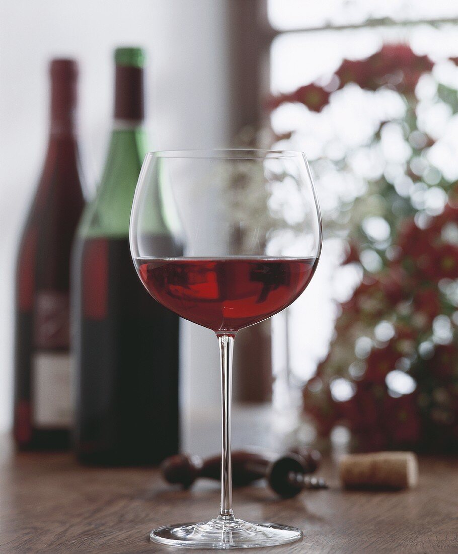 Ein Glas Rotwein, im Hintergrund Rotweinflaschen