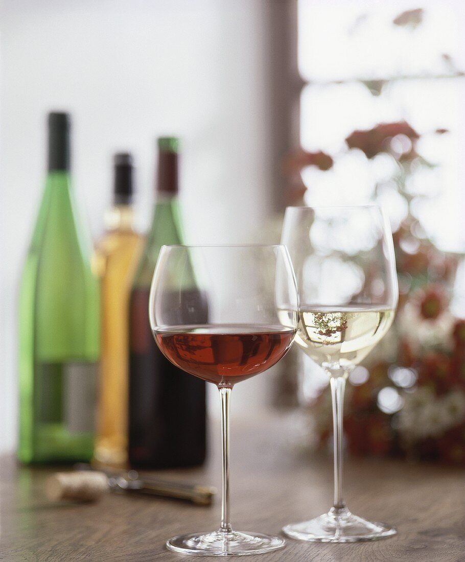 Glasses of red and white wine, wine bottles in background