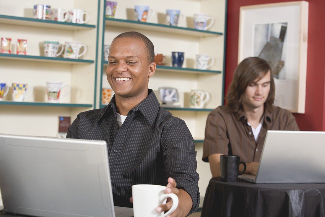 Zwei junge Männer an ihren Laptops in einem Café