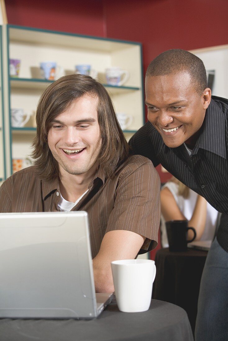 Zwei Männer im Café blicken interressiert auf einen Laptop