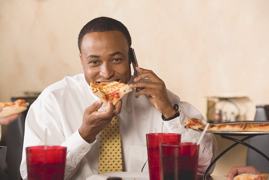 Geschäftsmann isst Pizza und telefoniert im Restaurant