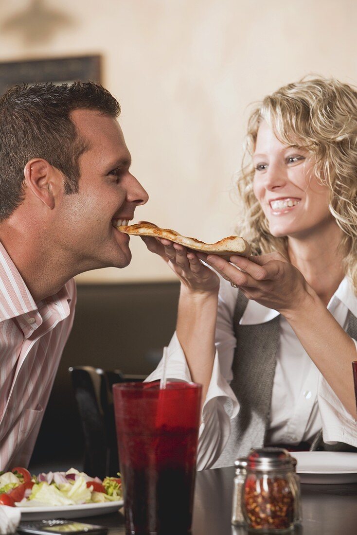 Woman feeding man pizza in restaurant