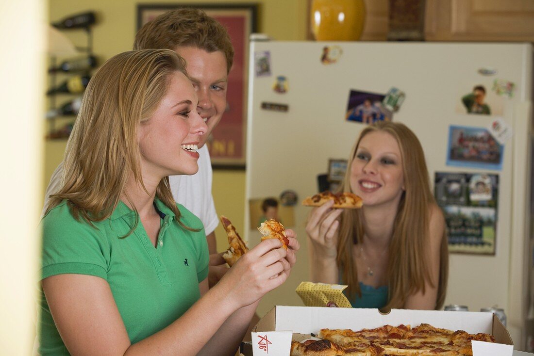 Three young people eating pizza