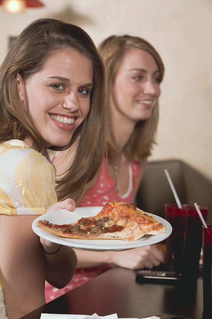 Two young women, one holding a plate of pizza